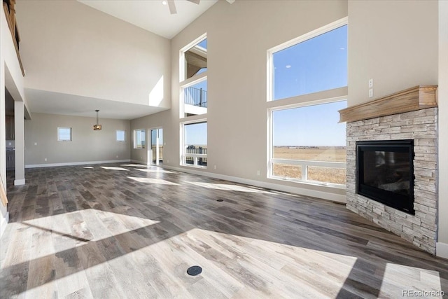 unfurnished living room featuring a high ceiling, wood-type flooring, a stone fireplace, and ceiling fan