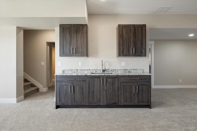 kitchen with light stone countertops, dark brown cabinets, sink, and light colored carpet