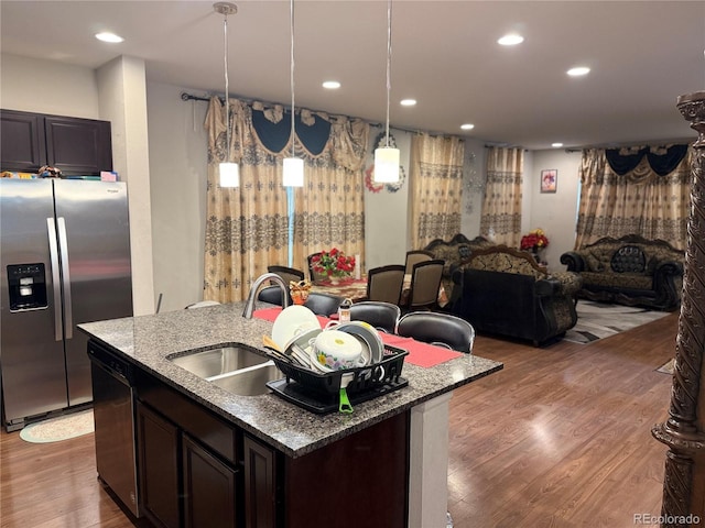 kitchen featuring dishwasher, a kitchen island with sink, dark brown cabinetry, pendant lighting, and stainless steel fridge