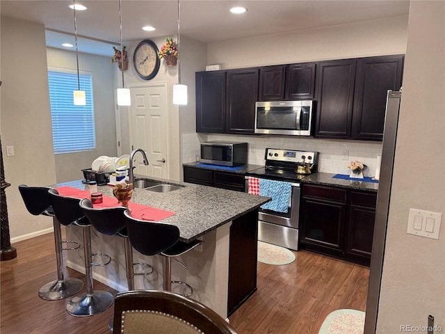 kitchen featuring appliances with stainless steel finishes, decorative backsplash, sink, hanging light fixtures, and a kitchen breakfast bar