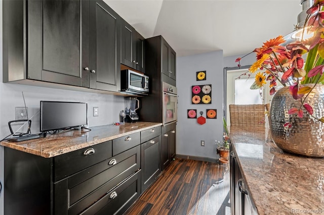 kitchen with stone counters, lofted ceiling, appliances with stainless steel finishes, and dark hardwood / wood-style flooring