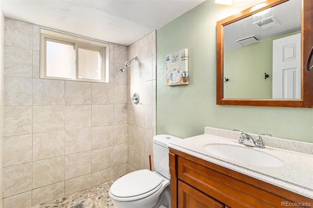 bathroom featuring a tile shower, vanity, and toilet