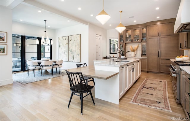 kitchen featuring high end stainless steel range oven, custom exhaust hood, an island with sink, and decorative light fixtures