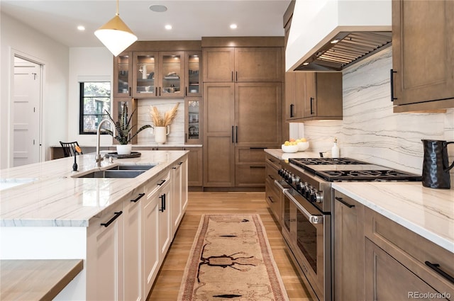 kitchen featuring sink, premium range hood, an island with sink, pendant lighting, and stainless steel stove