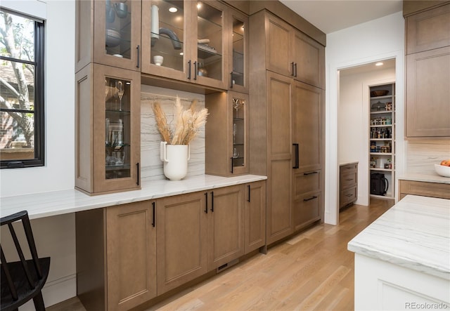 kitchen with decorative backsplash, light stone countertops, light hardwood / wood-style flooring, and built in desk