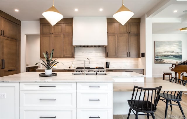 kitchen with premium range hood, decorative backsplash, white cabinetry, and hanging light fixtures