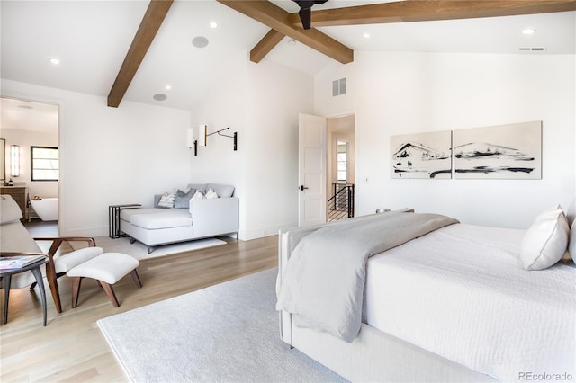 bedroom featuring vaulted ceiling with beams, light hardwood / wood-style floors, and ensuite bath