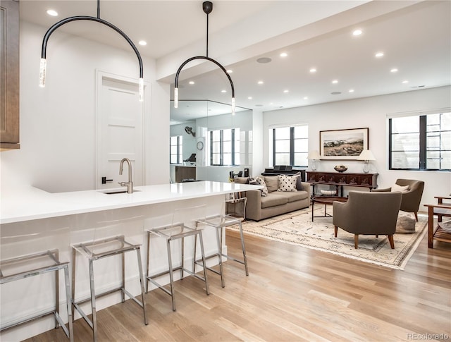 kitchen featuring a kitchen breakfast bar, light wood-type flooring, hanging light fixtures, and sink