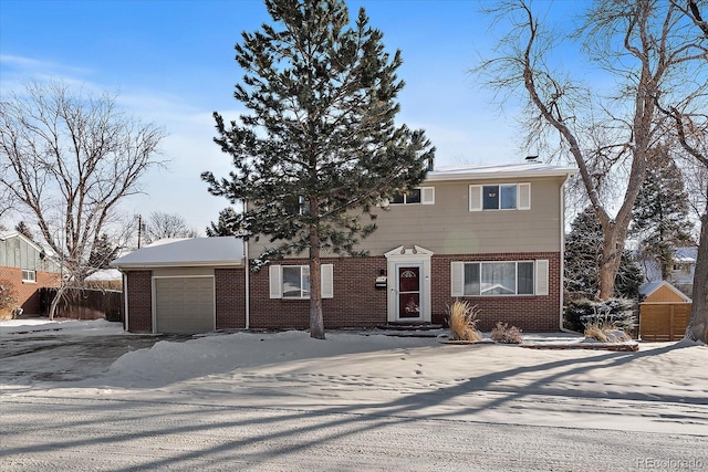 view of front facade featuring an attached garage, fence, brick siding, and driveway