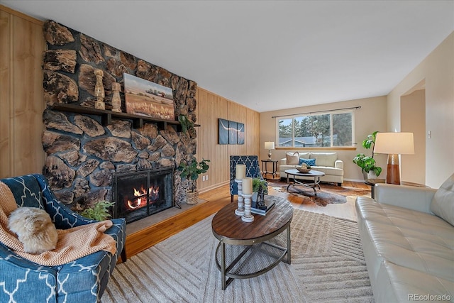 living area featuring a stone fireplace, wooden walls, and wood finished floors