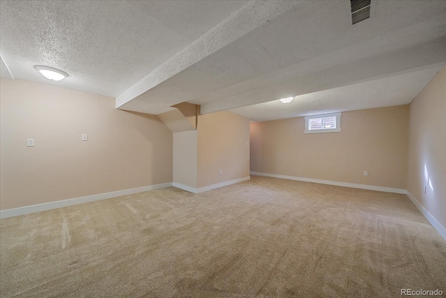 basement featuring a textured ceiling, visible vents, baseboards, and light carpet