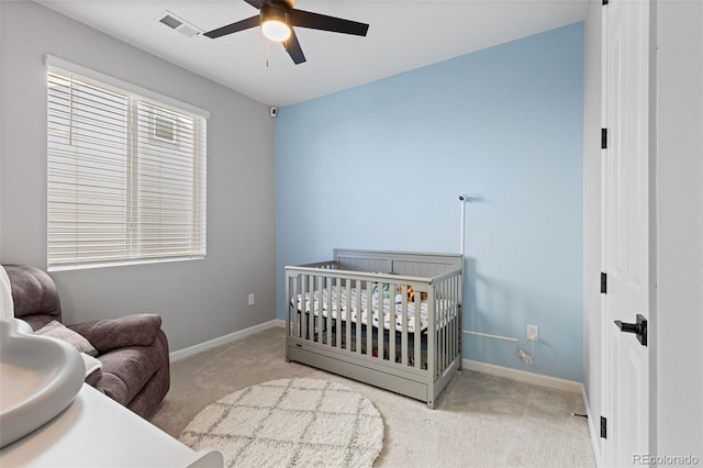 bedroom with light colored carpet, ceiling fan, and a nursery area