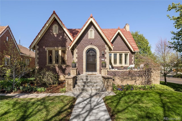 tudor-style house with a chimney, a front yard, and brick siding
