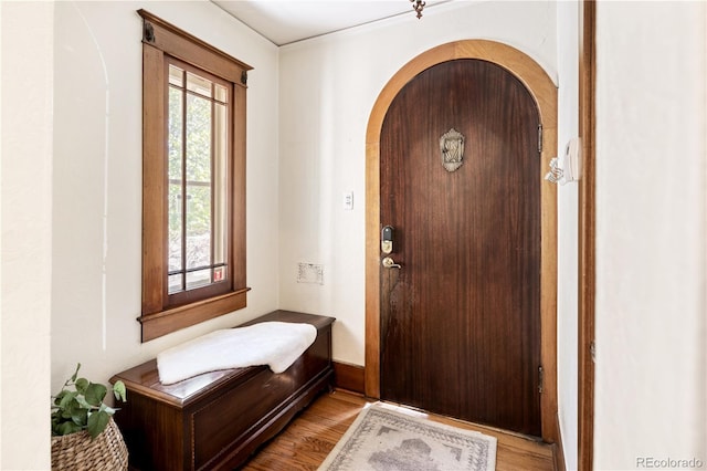 entryway with light wood finished floors, crown molding, and arched walkways