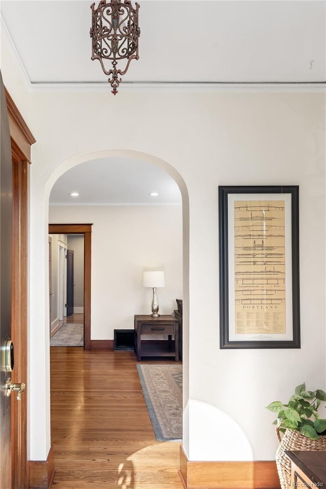 corridor with recessed lighting, baseboards, ornamental molding, wood finished floors, and arched walkways