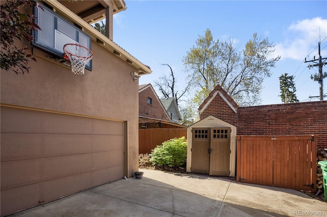 garage with fence, a storage shed, and concrete driveway