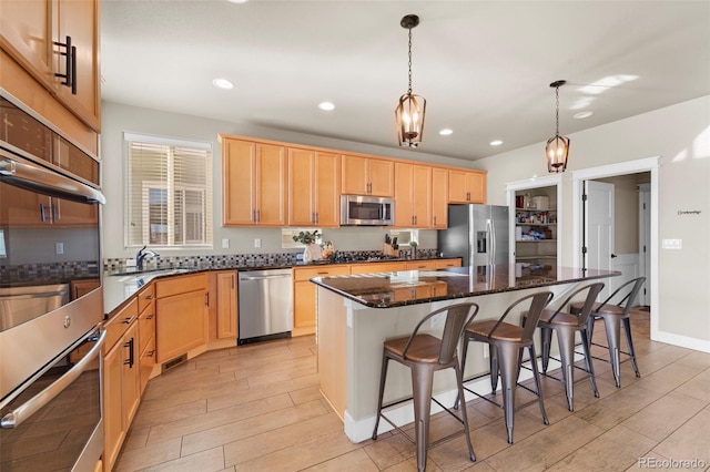 kitchen with appliances with stainless steel finishes, sink, dark stone countertops, hanging light fixtures, and a center island