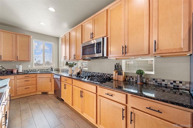 kitchen with stainless steel appliances, sink, dark stone countertops, and light brown cabinetry