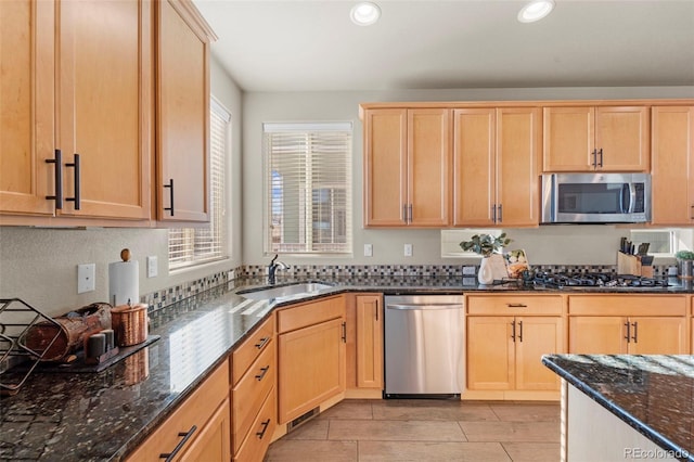 kitchen featuring stainless steel appliances, sink, light brown cabinets, and dark stone counters