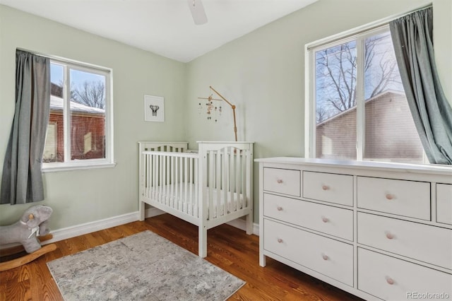 bedroom featuring ceiling fan, a nursery area, and dark hardwood / wood-style flooring