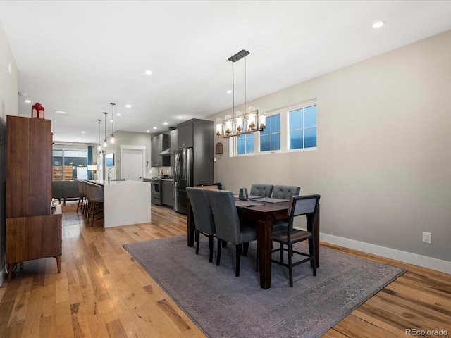 dining area with sink, an inviting chandelier, and light wood-type flooring