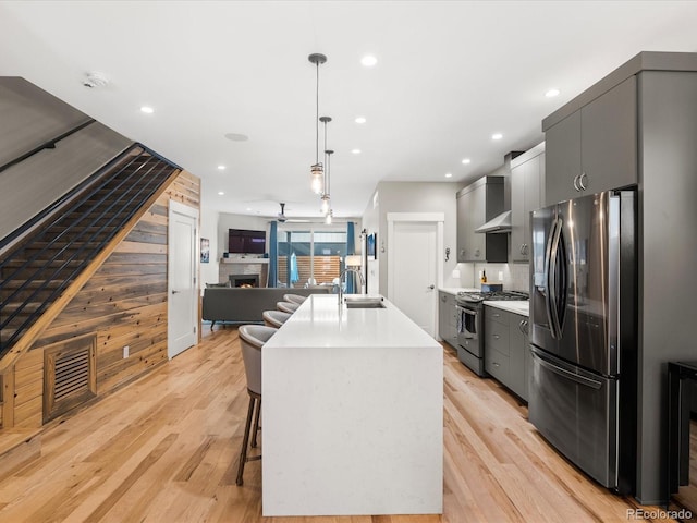 kitchen with appliances with stainless steel finishes, gray cabinetry, an island with sink, a kitchen bar, and decorative light fixtures