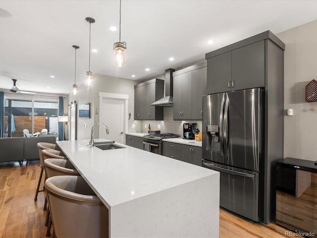 kitchen with sink, a kitchen breakfast bar, stainless steel refrigerator with ice dispenser, gas range oven, and wall chimney exhaust hood