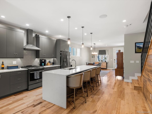 kitchen featuring pendant lighting, wall chimney range hood, a kitchen island with sink, stainless steel appliances, and a kitchen breakfast bar