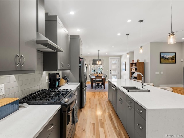 kitchen with gas stove, decorative light fixtures, stainless steel fridge, gray cabinets, and wall chimney range hood