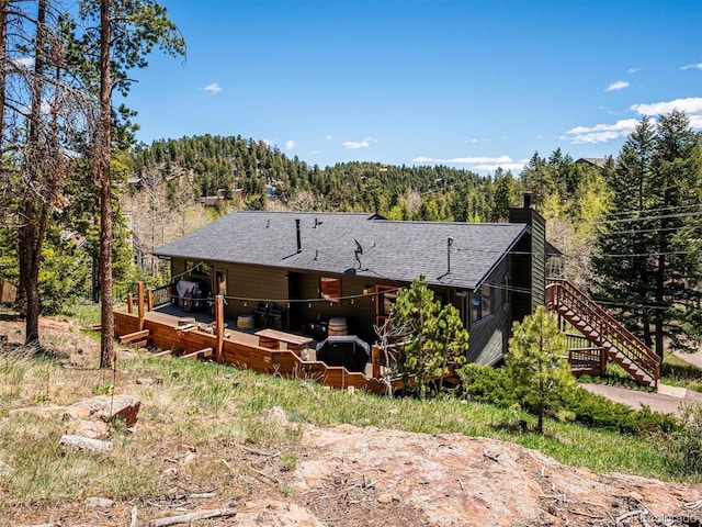34075 Grouse Ln, Evergreen, CO 80439 - back of property featuring a chimney, a deck, a wooded view, and a shingled roof