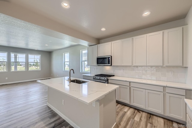 kitchen with tasteful backsplash, an island with sink, appliances with stainless steel finishes, light wood-style floors, and a sink