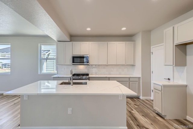 kitchen featuring light wood-style flooring, stainless steel appliances, a sink, decorative backsplash, and light stone countertops