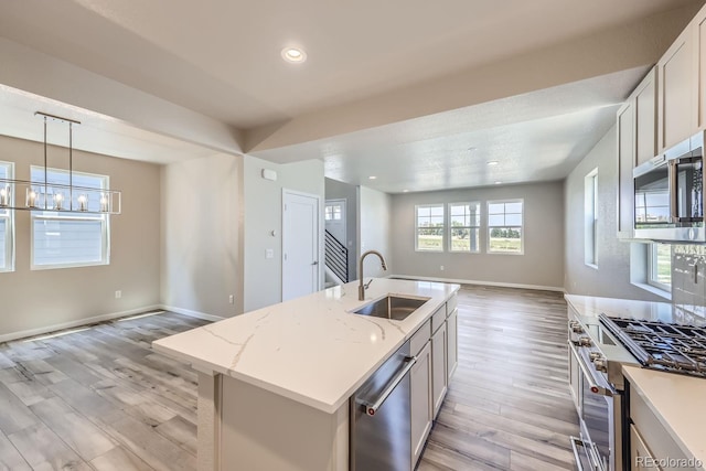 kitchen with stainless steel appliances, open floor plan, a sink, light wood-type flooring, and baseboards