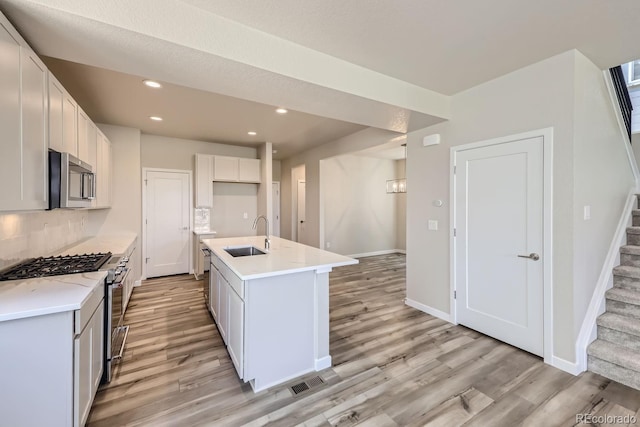 kitchen with baseboards, light wood-style flooring, appliances with stainless steel finishes, a sink, and recessed lighting