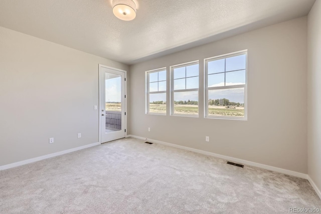 empty room with baseboards, light colored carpet, visible vents, and a textured ceiling