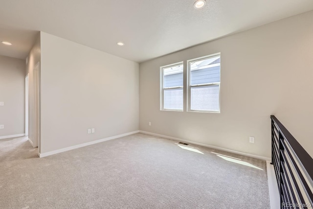 spare room featuring recessed lighting, light colored carpet, and baseboards