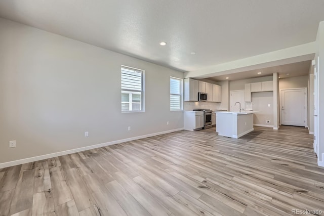 unfurnished living room featuring light wood-style floors, baseboards, a sink, and recessed lighting