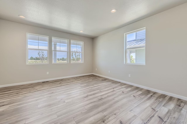 spare room with recessed lighting, baseboards, a textured ceiling, and light wood finished floors