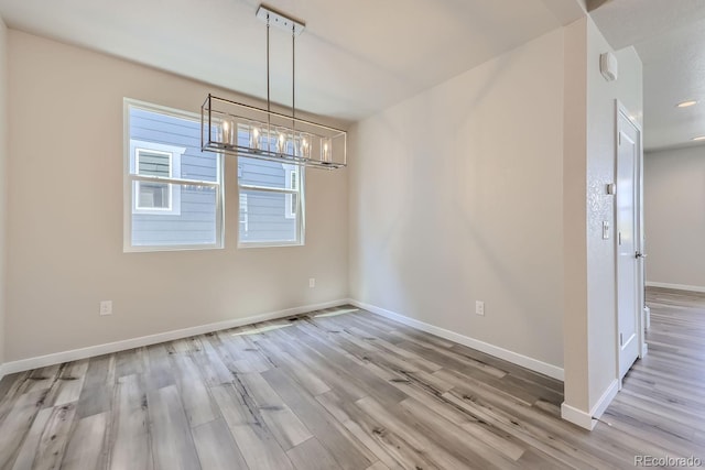 unfurnished dining area featuring an inviting chandelier, baseboards, and wood finished floors