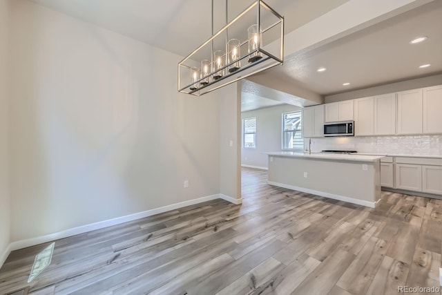 kitchen featuring light countertops, stainless steel microwave, backsplash, light wood-type flooring, and baseboards