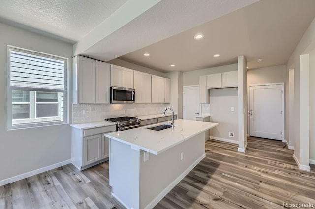 kitchen featuring light wood finished floors, baseboards, decorative backsplash, appliances with stainless steel finishes, and a sink