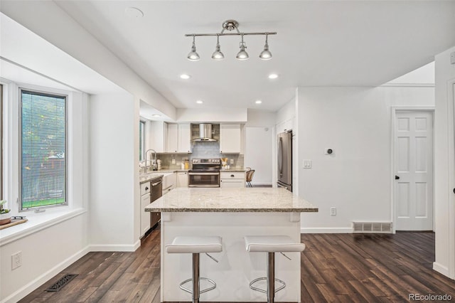 13701 Yank Way, Arvada, CO 80004 - kitchen featuring stainless steel appliances, wall chimney exhaust hood, dark wood-style floors, white cabinets, and light stone counters