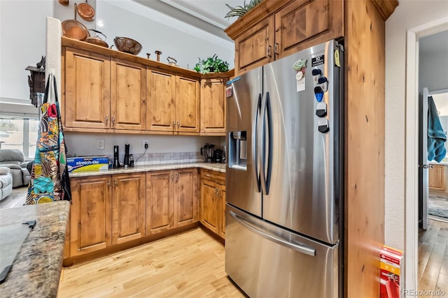 kitchen with stainless steel refrigerator with ice dispenser, light wood finished floors, light stone countertops, and brown cabinetry