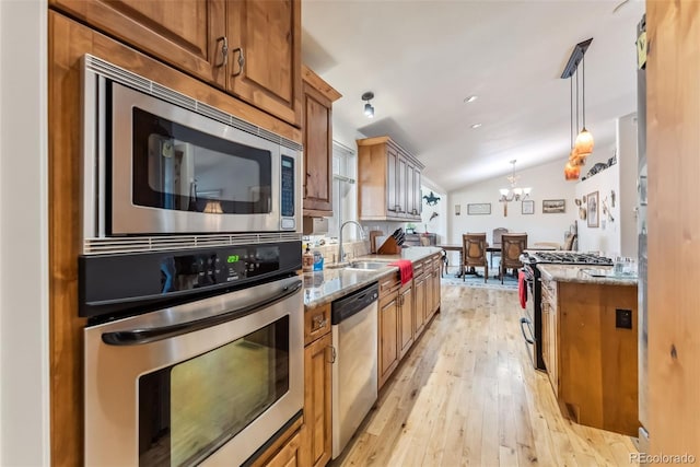 kitchen featuring stainless steel appliances, vaulted ceiling, brown cabinets, a chandelier, and light wood finished floors