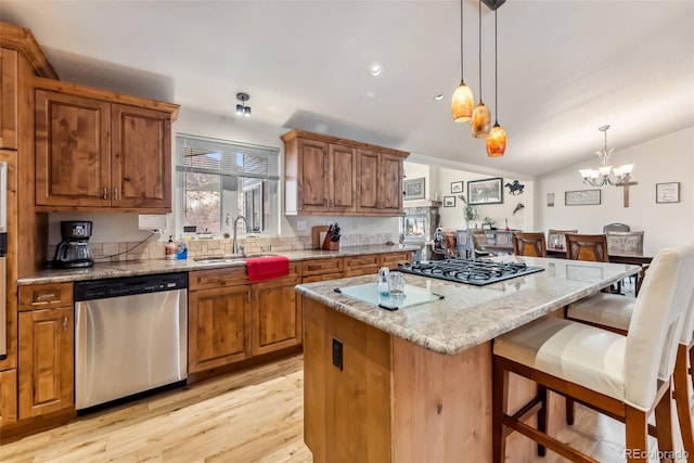 kitchen featuring appliances with stainless steel finishes, a sink, brown cabinetry, light wood-type flooring, and vaulted ceiling
