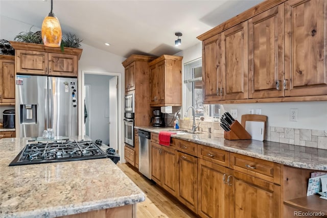kitchen with stainless steel appliances, a sink, brown cabinetry, and vaulted ceiling