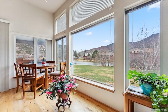 sunroom / solarium featuring hardwood / wood-style floors, a water and mountain view, plenty of natural light, and a towering ceiling