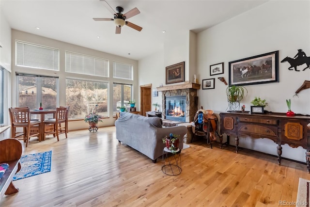 living area with a fireplace, ceiling fan, light wood-style flooring, a high ceiling, and recessed lighting