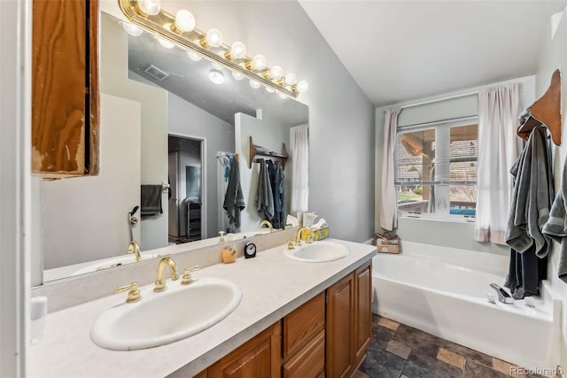 bathroom featuring stone finish flooring, a bath, and double vanity