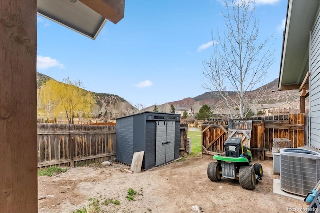 fenced backyard with a storage shed, cooling unit, a mountain view, and an outdoor structure